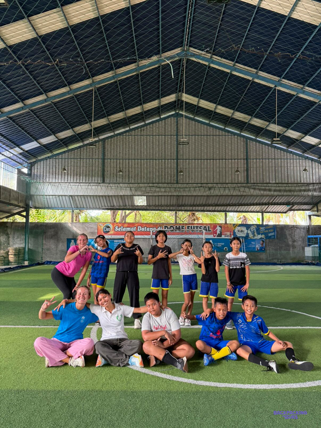 Volunteers and children pose together for a team photo on an indoor futsal pitch.