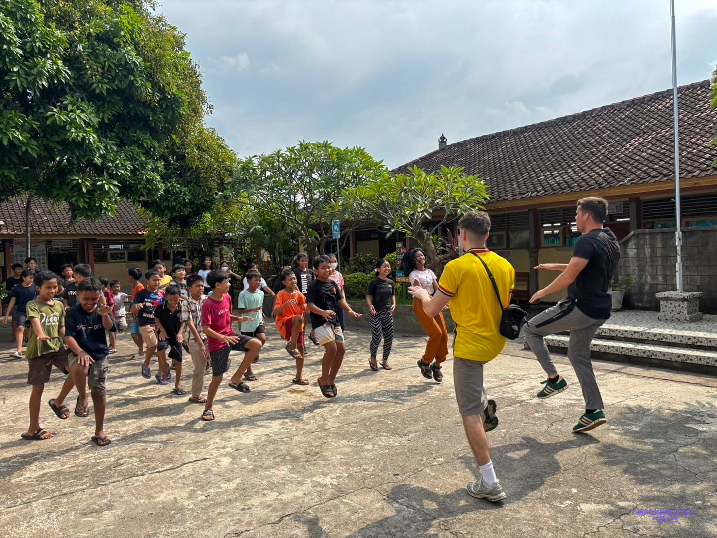 Two volunteer coaches lead a crowd of schoolchildren through warm-up exercises in the playground.