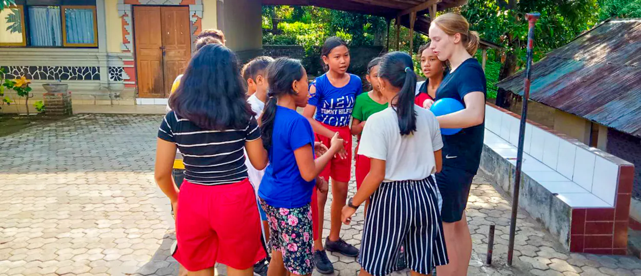 A volunteer holds a blue ball as she talks with a group of girls in the schoolyard.