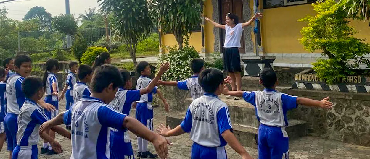 Boys in blue and white football kit hold hands in a circle in the schoolyard.