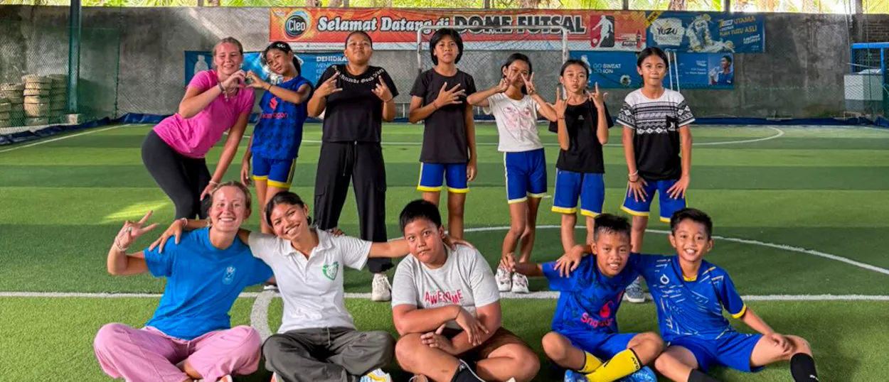 Volunteers and children pose together for a team photo on an indoor futsal pitch.