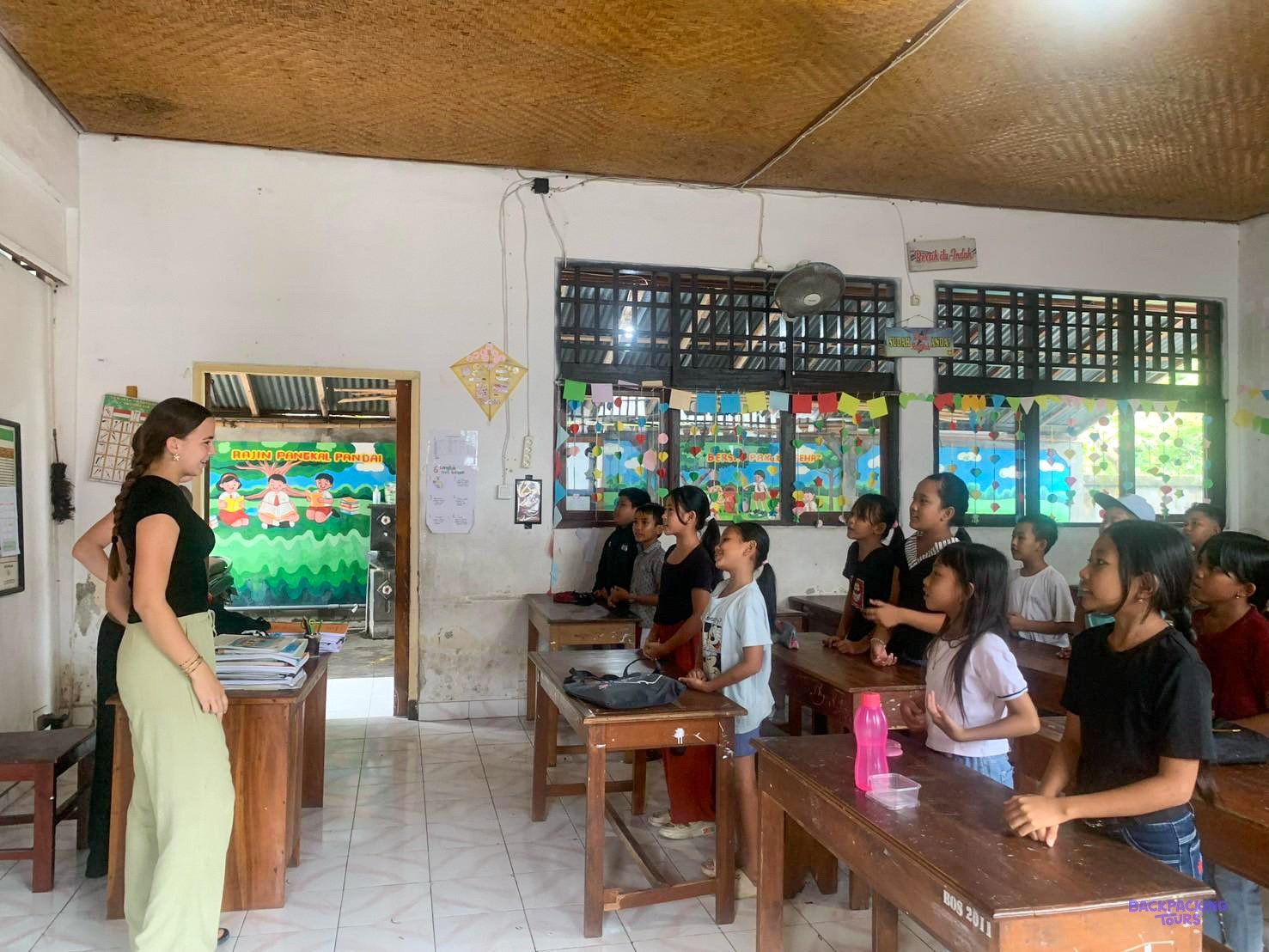 A volunteer stands at the front of a bright classroom, teaching a full class of children.