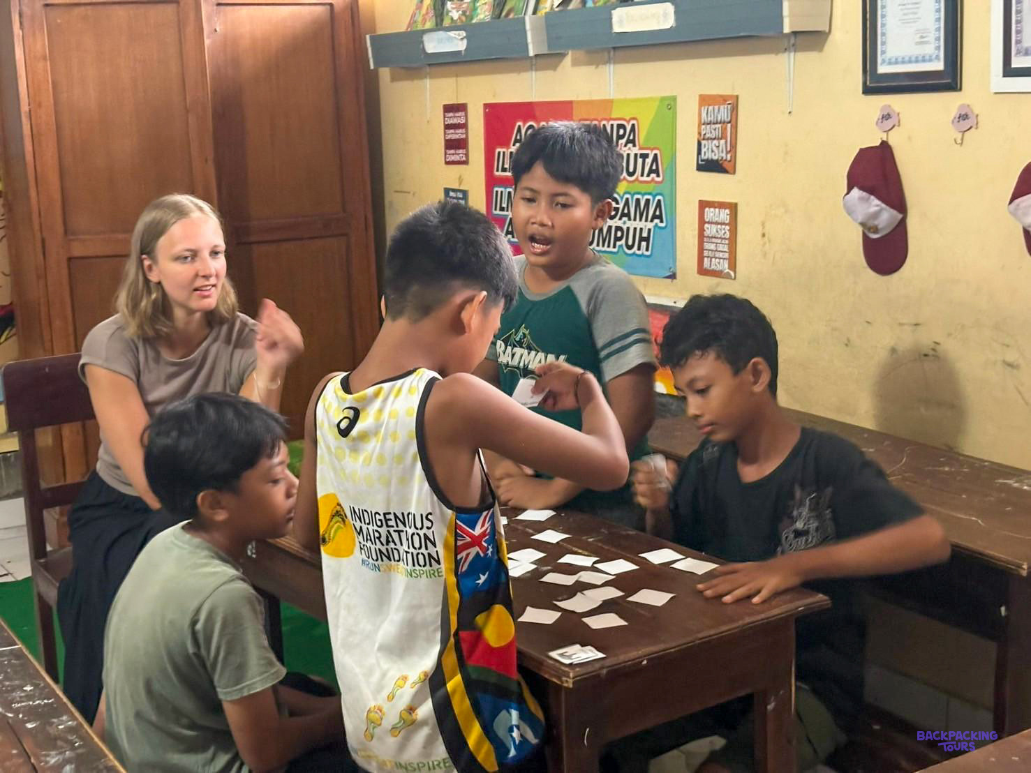A volunteer plays an English word-card game with a group of boys around a desk.