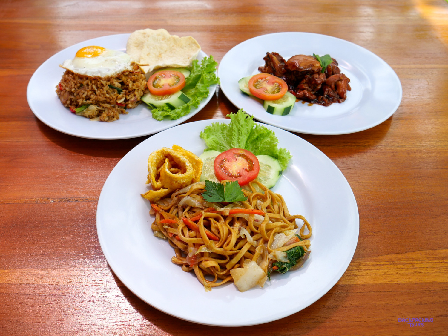 Three plates of Indonesian food: fried noodles, fried rice with an egg, and a meat dish.