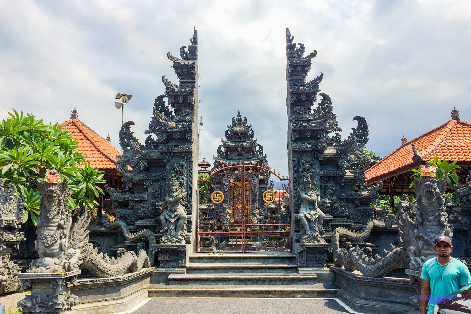 The carved stone split gateway of a Balinese temple, flanked by statues and red-tiled pavilions.