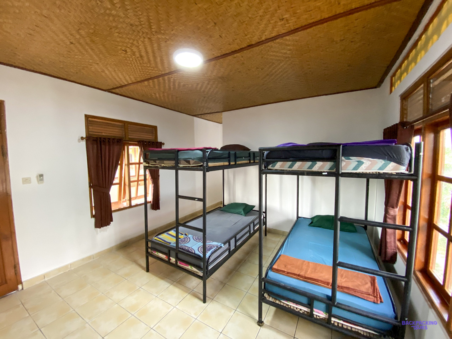 Two black metal bunk beds with fresh linen in a bright, tiled shared bedroom.