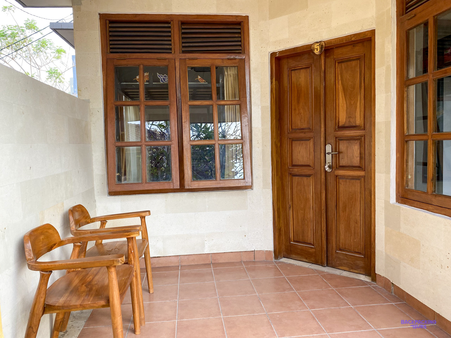 Two wooden chairs on a tiled porch outside a bedroom's carved wooden double doors.