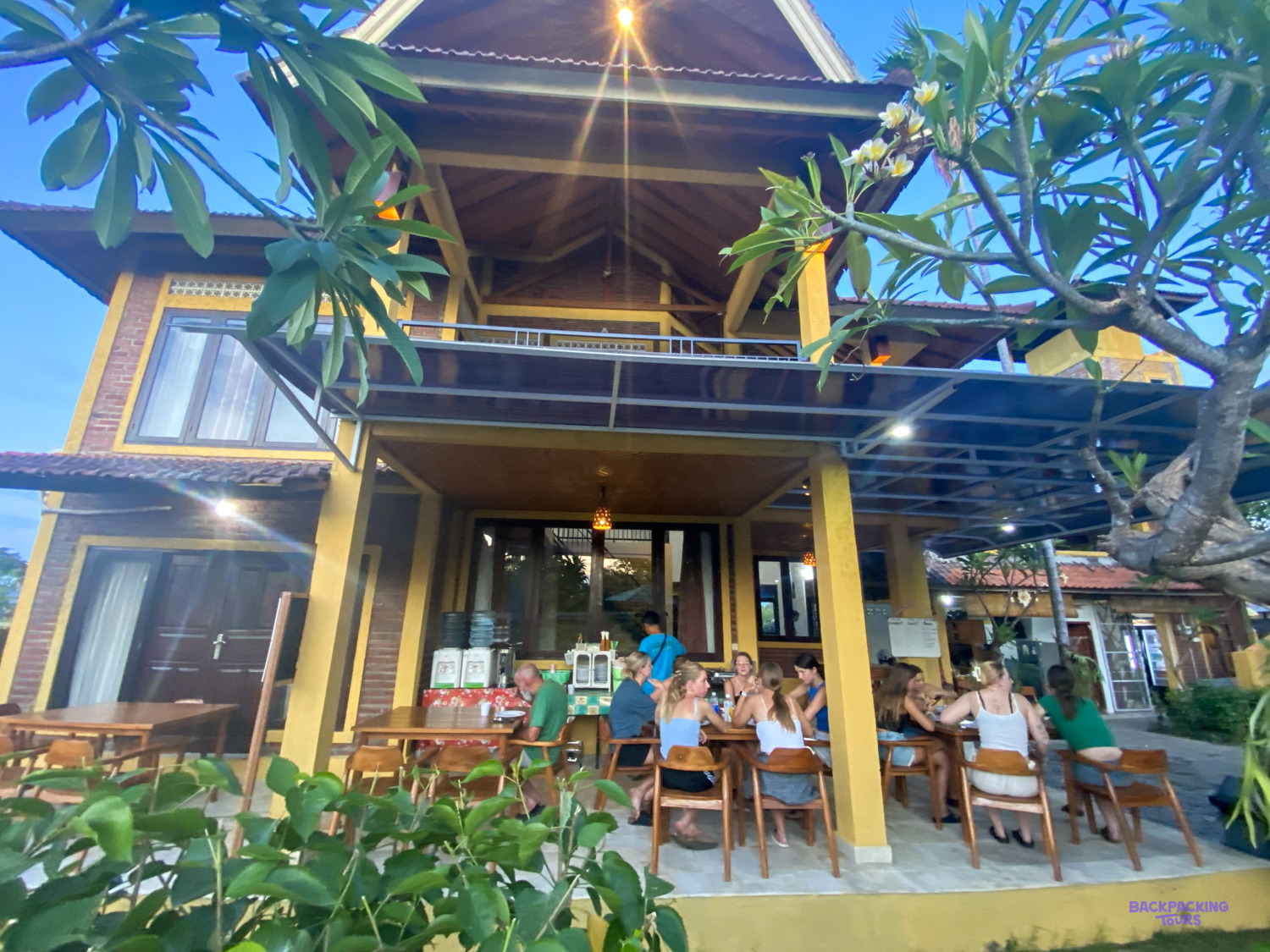 Volunteers eat together on the covered terrace of the two-storey volunteer house at dusk.