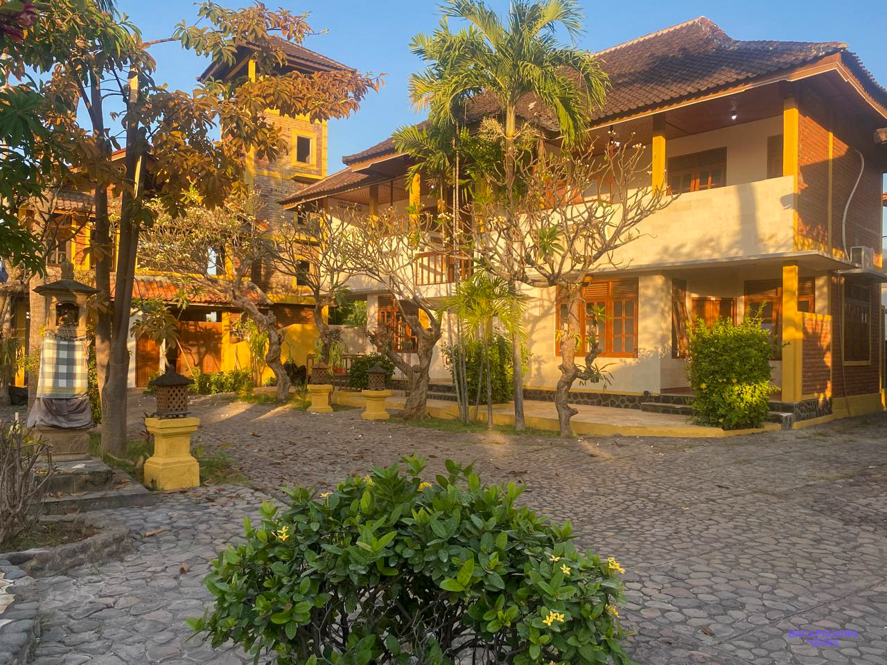 Low evening sun on the volunteer house's yellow-trimmed buildings around a cobbled courtyard.