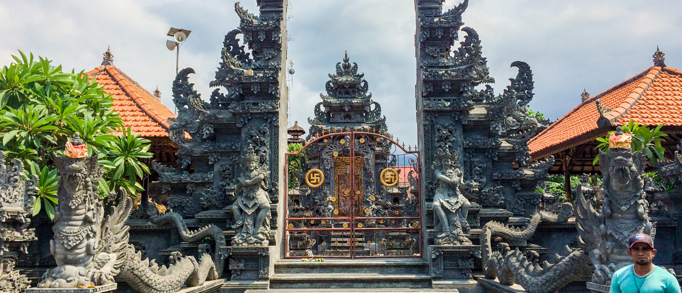 The carved stone split gateway of a Balinese temple, flanked by statues and red-tiled pavilions.