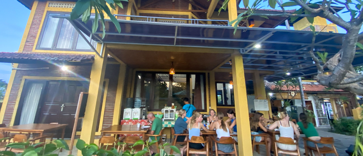 Volunteers eat together on the covered terrace of the two-storey volunteer house at dusk.