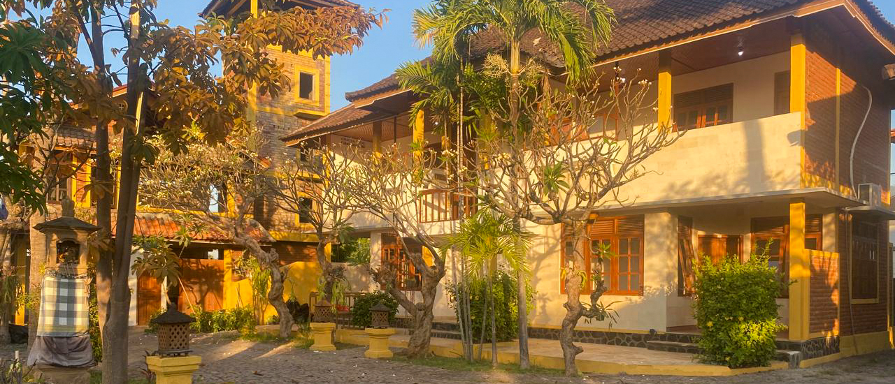 Low evening sun on the volunteer house's yellow-trimmed buildings around a cobbled courtyard.