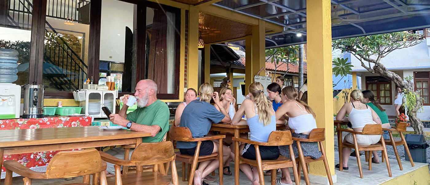 Volunteers chat over a meal at long wooden tables on the house's open terrace.