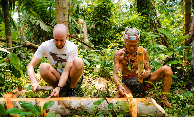A traveler learns traditional wood carving from a Mentawai tribesman in the Indonesian jungle.