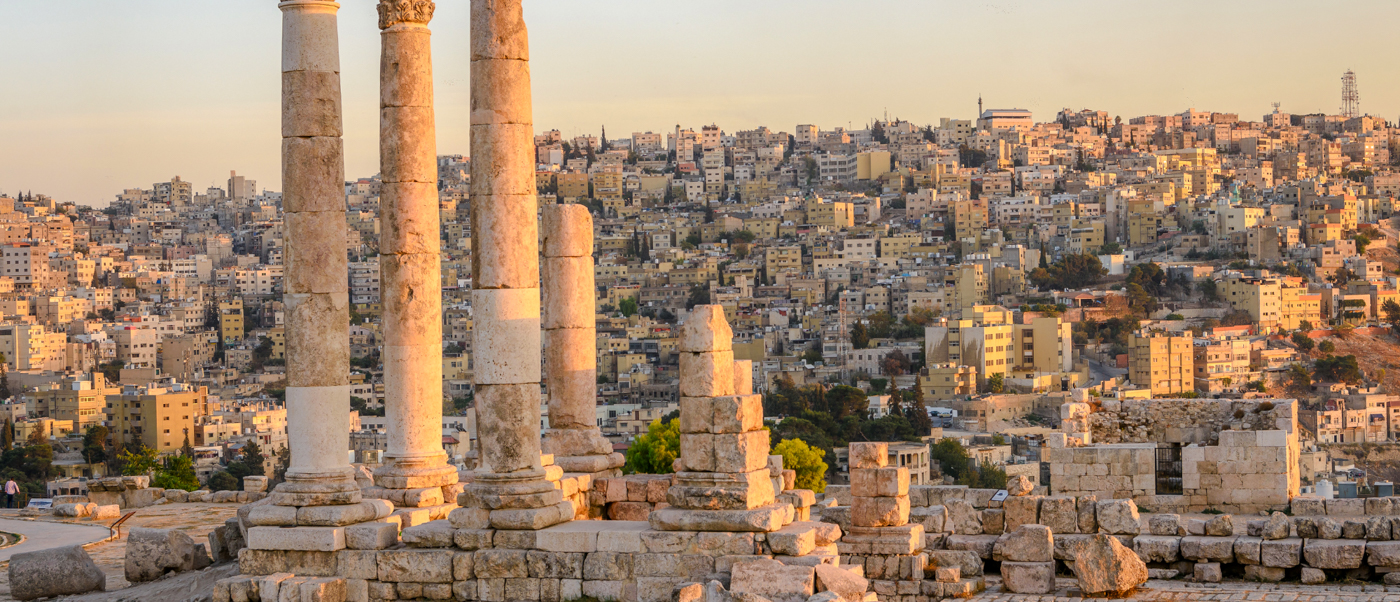 Ancient Roman columns overlook the sprawling city of Amman, Jordan, bathed in warm sunset light.