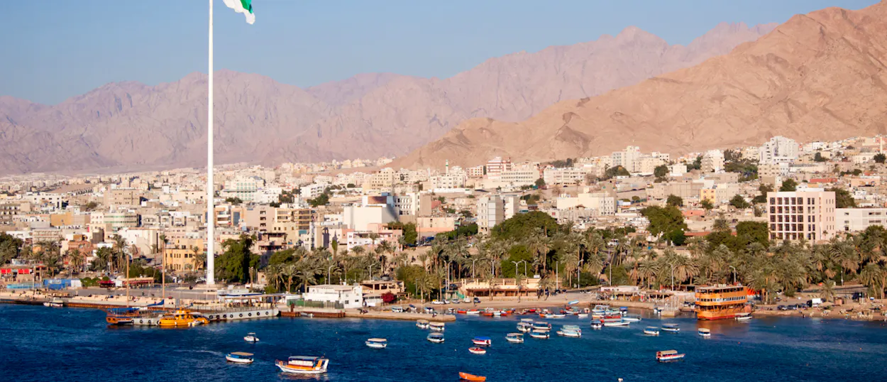 Aqaba, Jordan, a bustling coastal city with boats on the Red Sea and towering desert mountains.