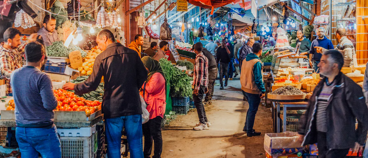 A vibrant market in Amman, Jordan, filled with people browsing stalls of fresh fruits and vegetables.
