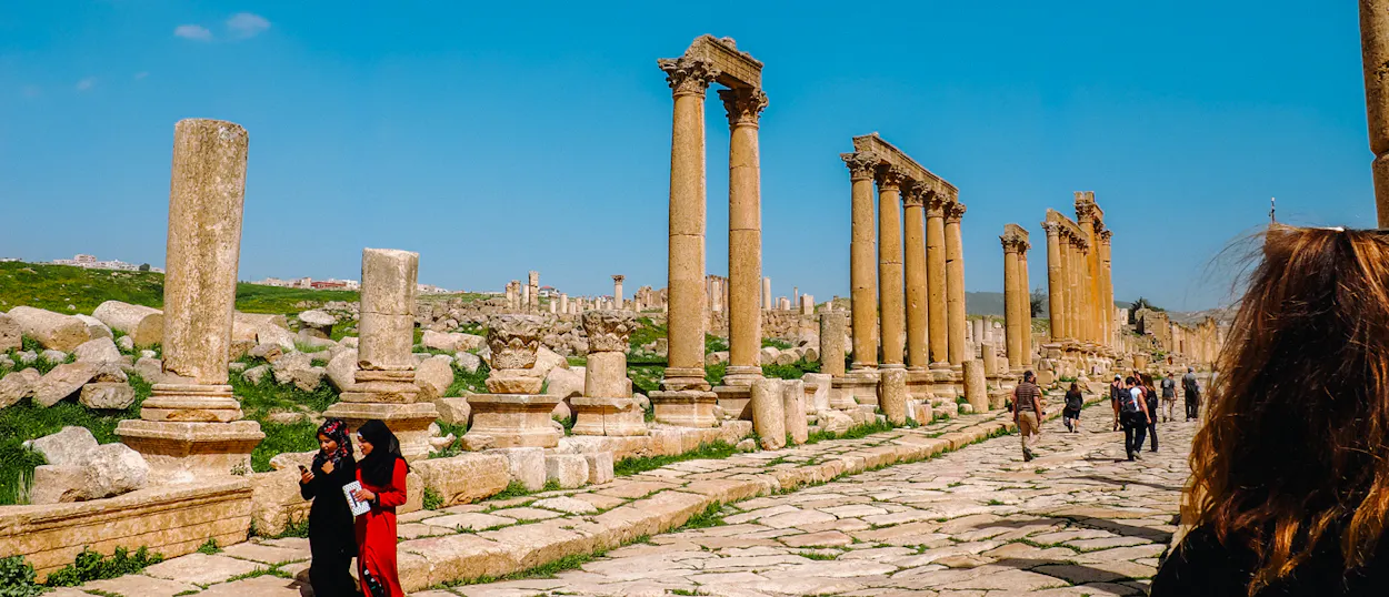 Travelers walk among the impressive Roman ruins and towering columns of ancient Jerash, Jordan.