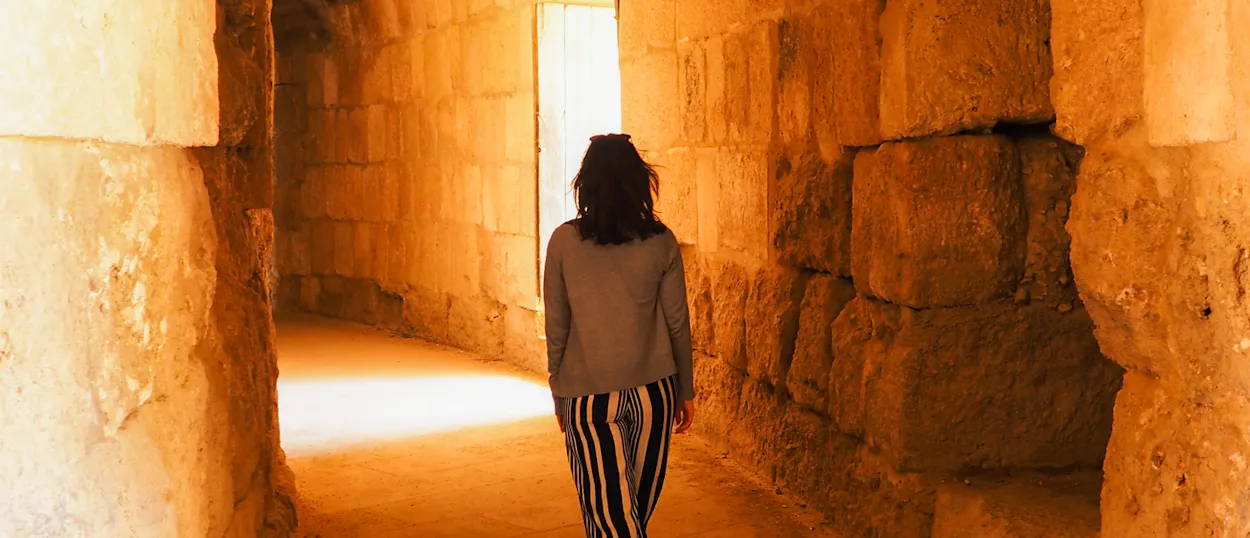 A person walks through a sunlit stone passageway within the ancient Jerash Roman ruins.