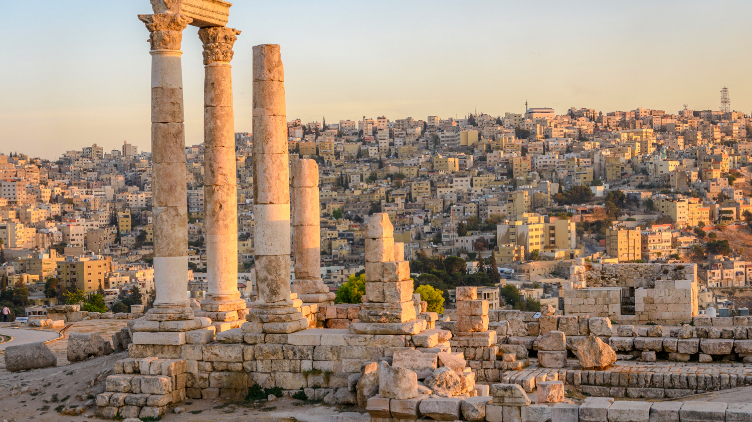 Ancient Roman columns stand tall over the sprawling city of Amman, Jordan at sunset.
