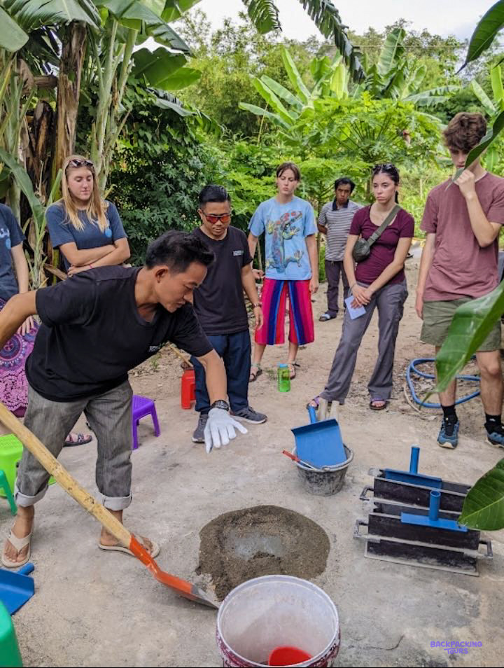 A local coordinator shows a group of volunteers how to mix cement with a shovel.