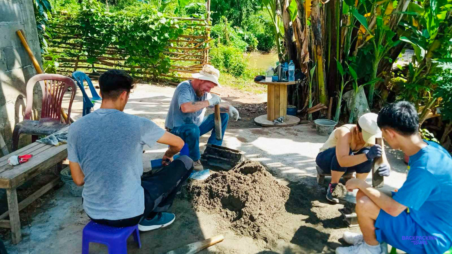 Volunteers crouch round a pile of cement, packing it into block moulds in a garden yard.