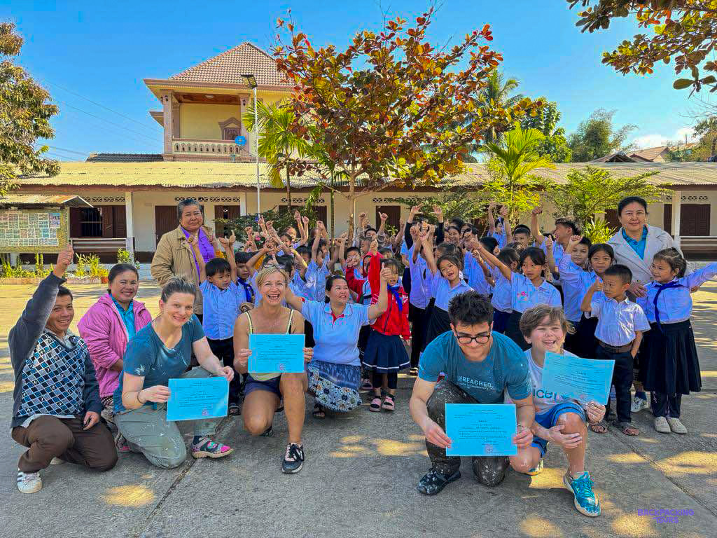 Volunteers hold certificates as cheering schoolchildren and teachers gather outside a Lao school.