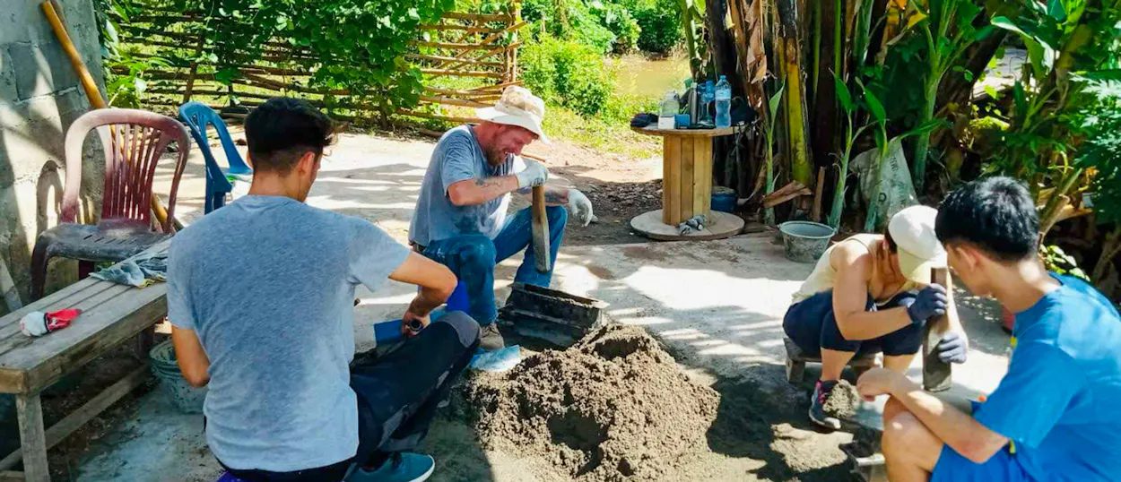 Volunteers crouch round a pile of cement, packing it into block moulds in a garden yard.