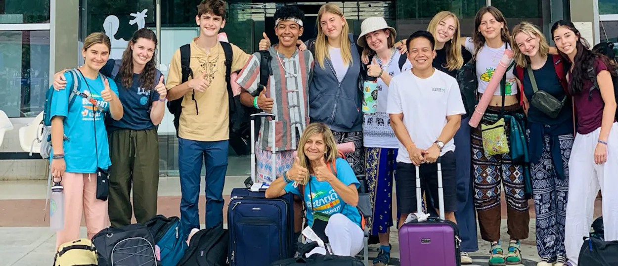 A smiling group of volunteers with their suitcases outside the airport terminal in Laos.