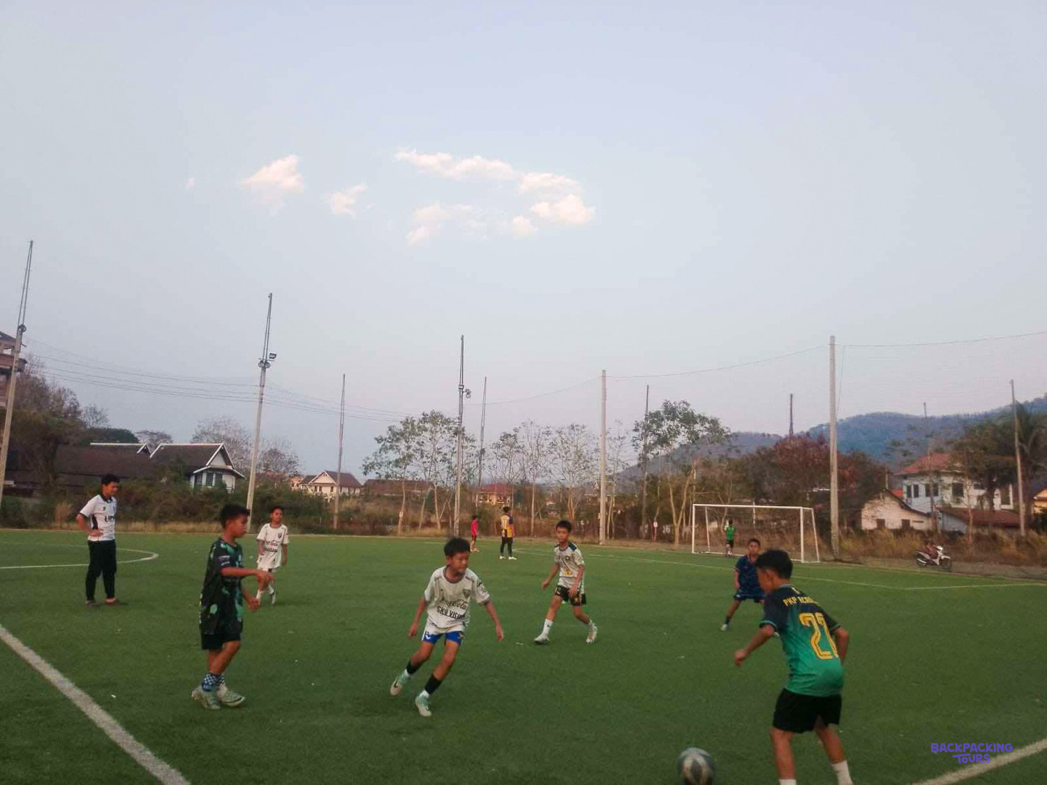 Young players in green and white kits battle for the ball during an evening training game.