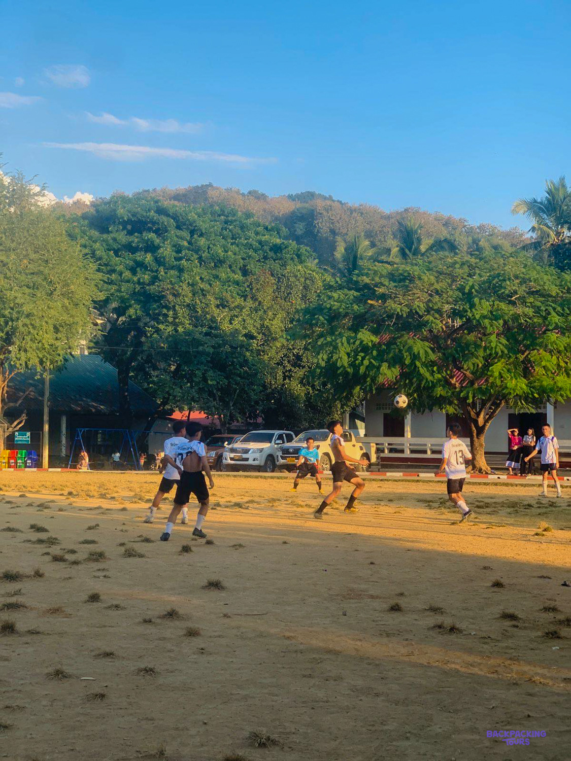 Boys chase a football across a dusty school pitch in the golden evening light in Luang Prabang.