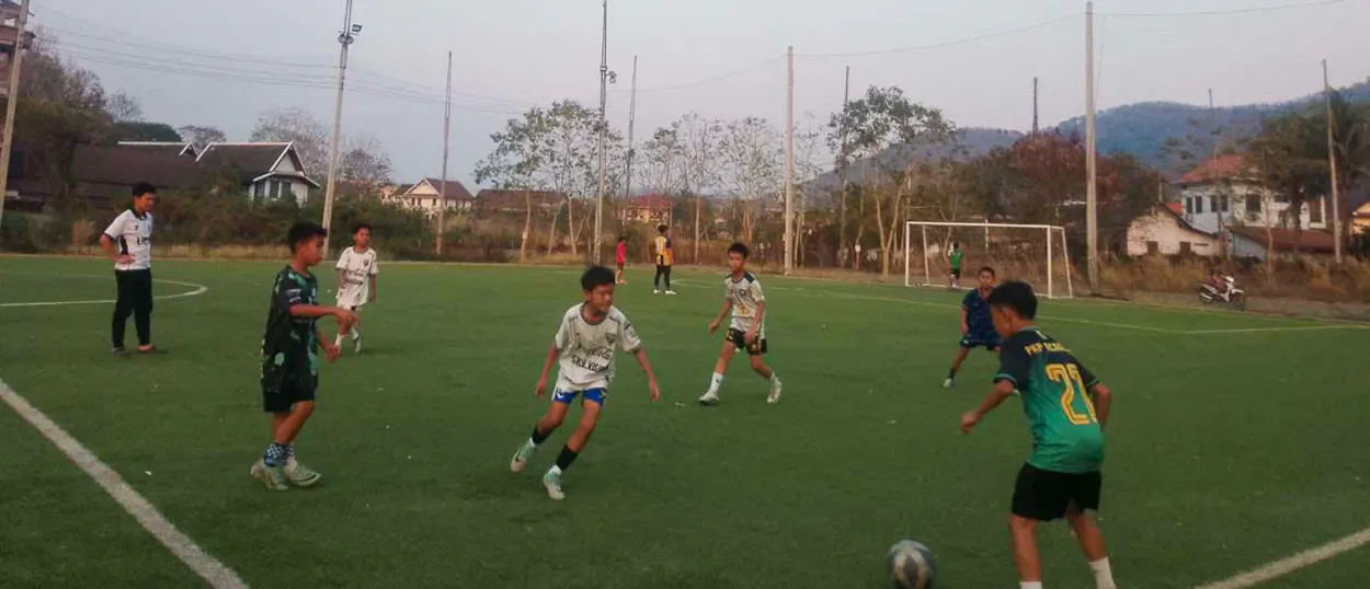 Young players in green and white kits battle for the ball during an evening training game.