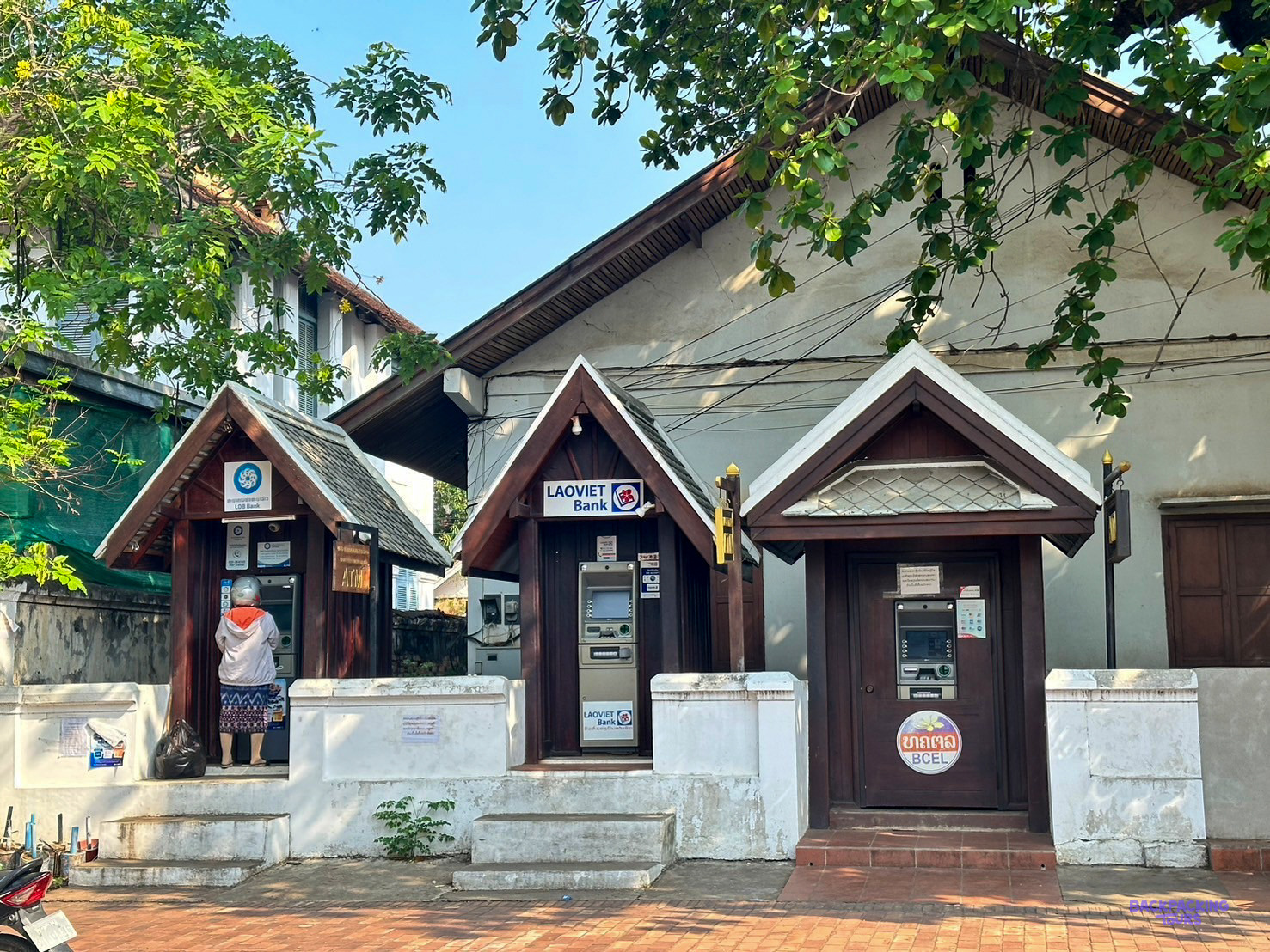 Three small wooden kiosks with cash machines stand in a row on a Luang Prabang street.
