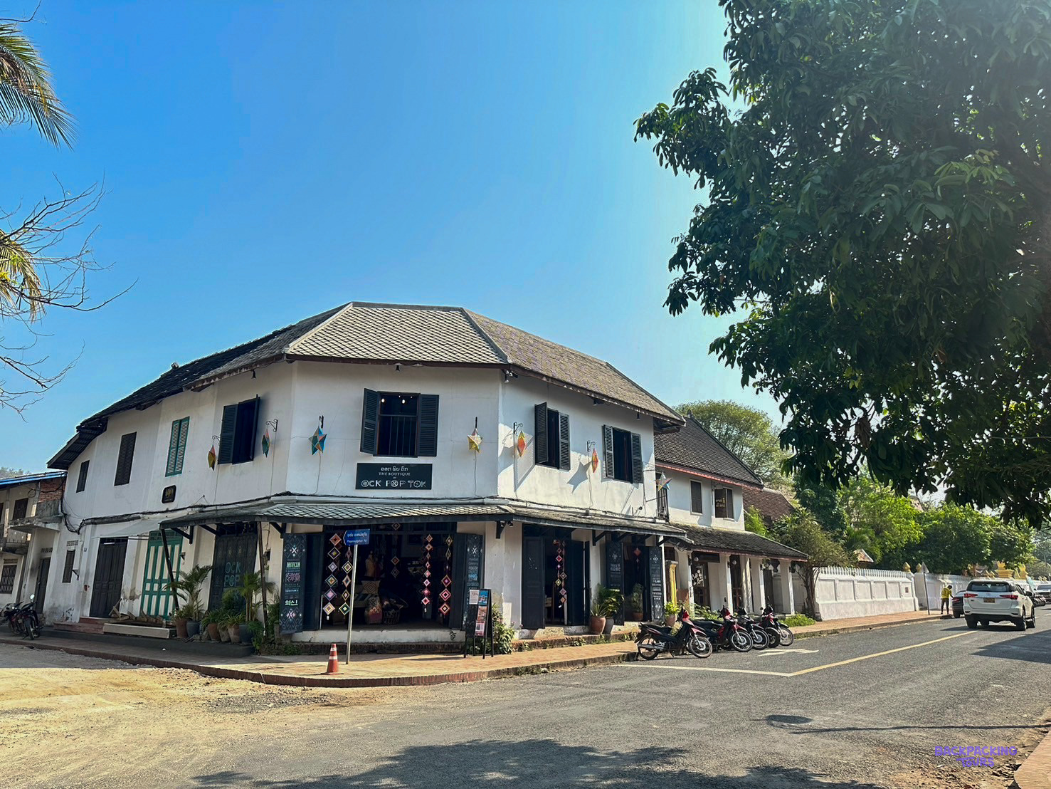 A white two-storey colonial shophouse on a quiet street corner in Luang Prabang's old town.