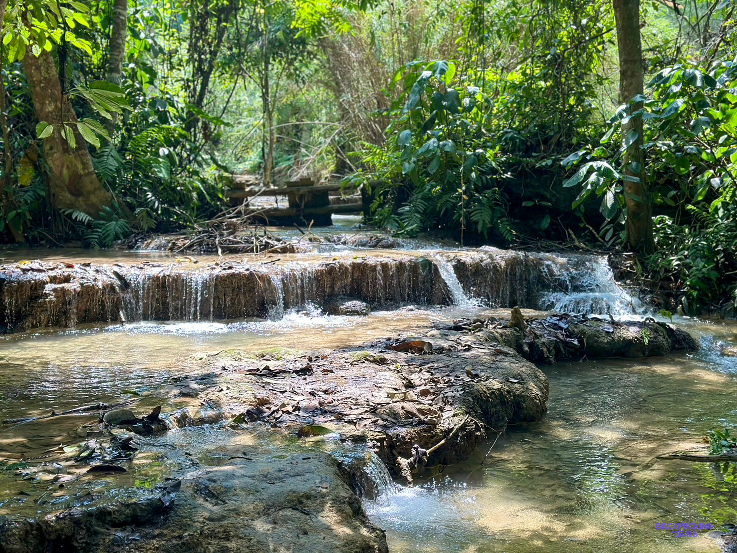 Shallow cascades tumble over limestone ledges beneath jungle trees outside Luang Prabang.