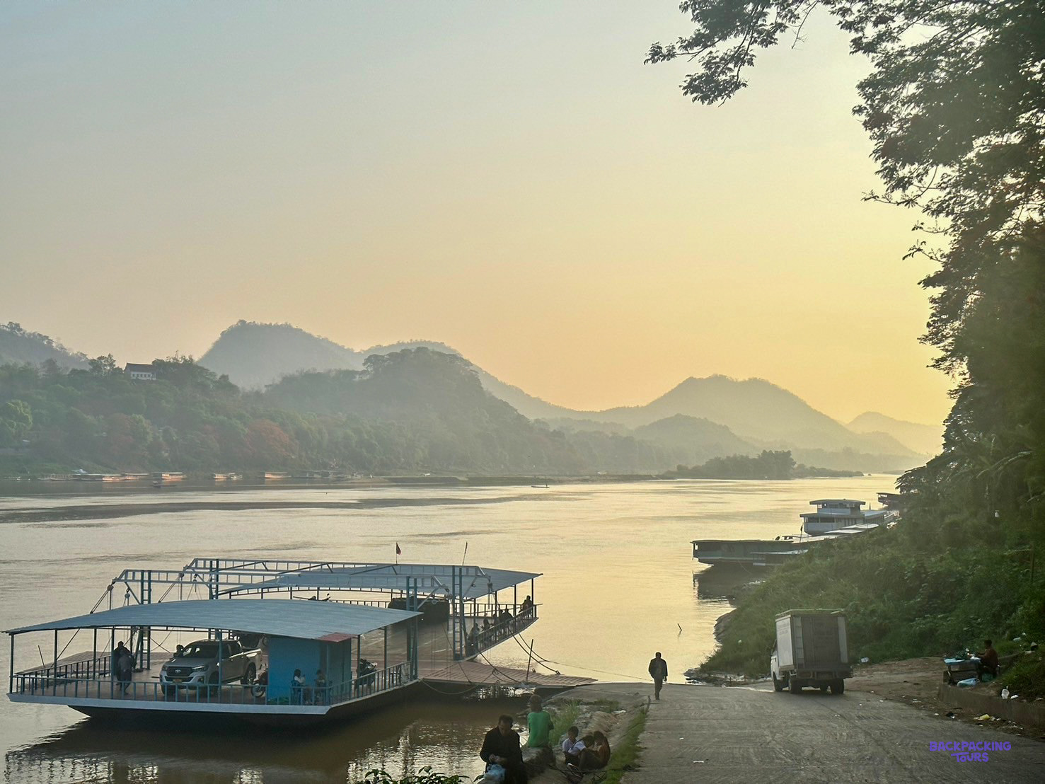 A car ferry waits at a slipway on the Mekong as mist settles over the hills beyond.