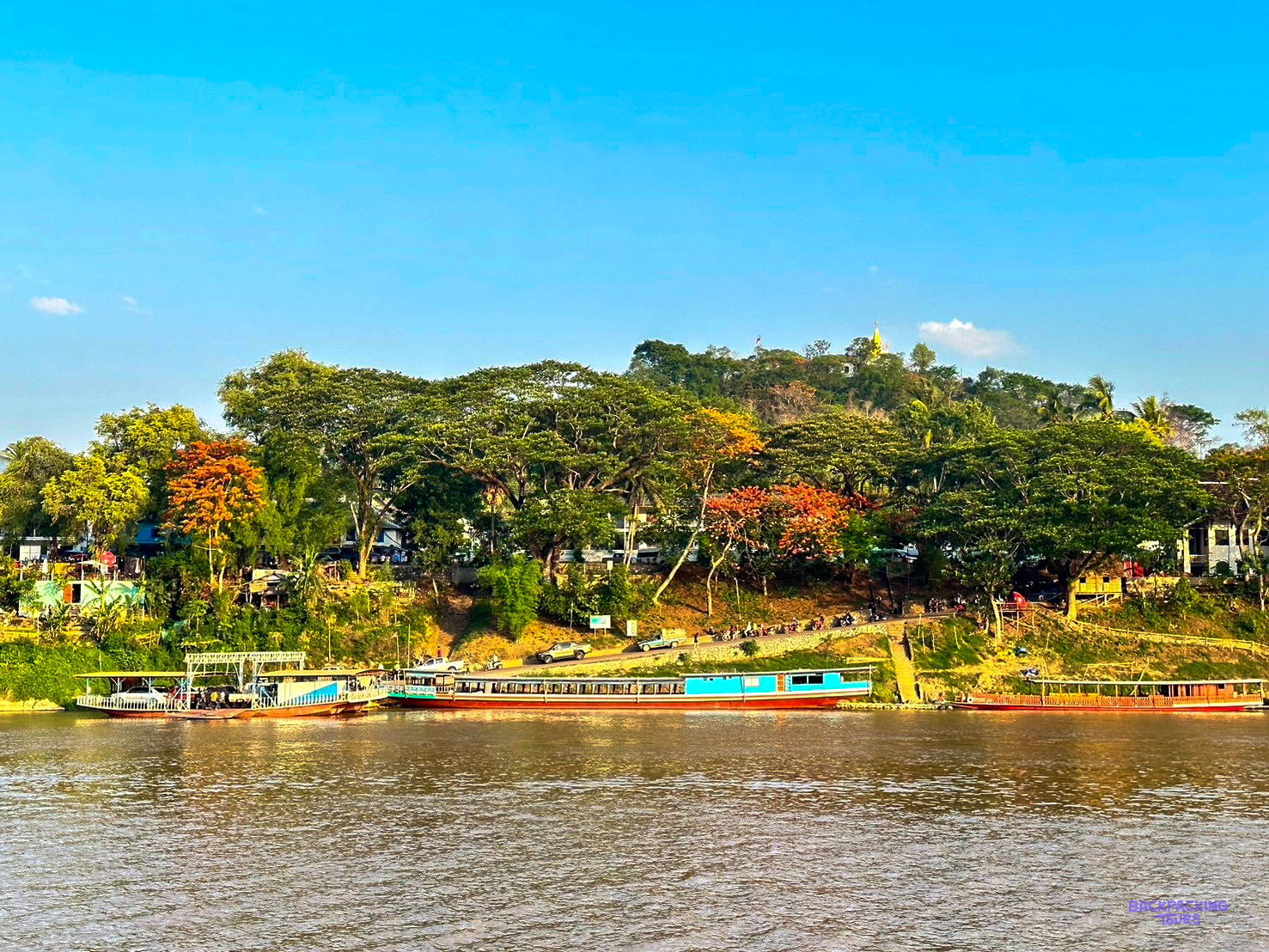 Colourful river boats wait below the wooded riverbank of Luang Prabang in the late afternoon light.