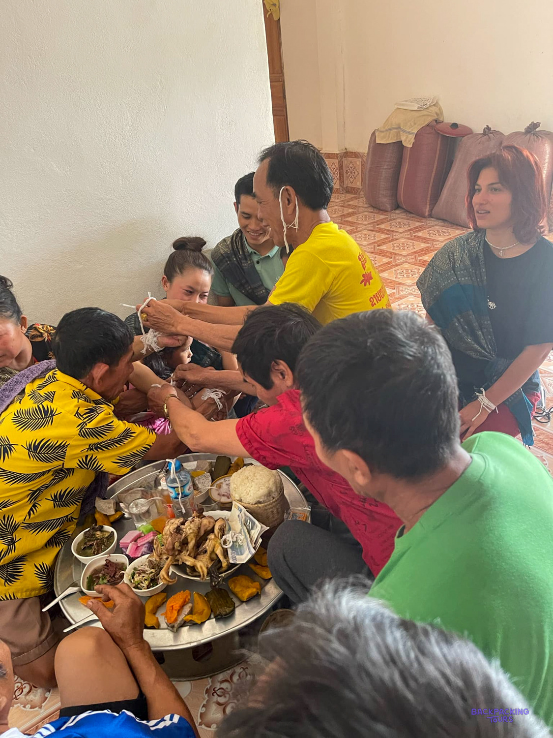 Volunteers and local people share a meal of many small dishes, sitting together on the floor.