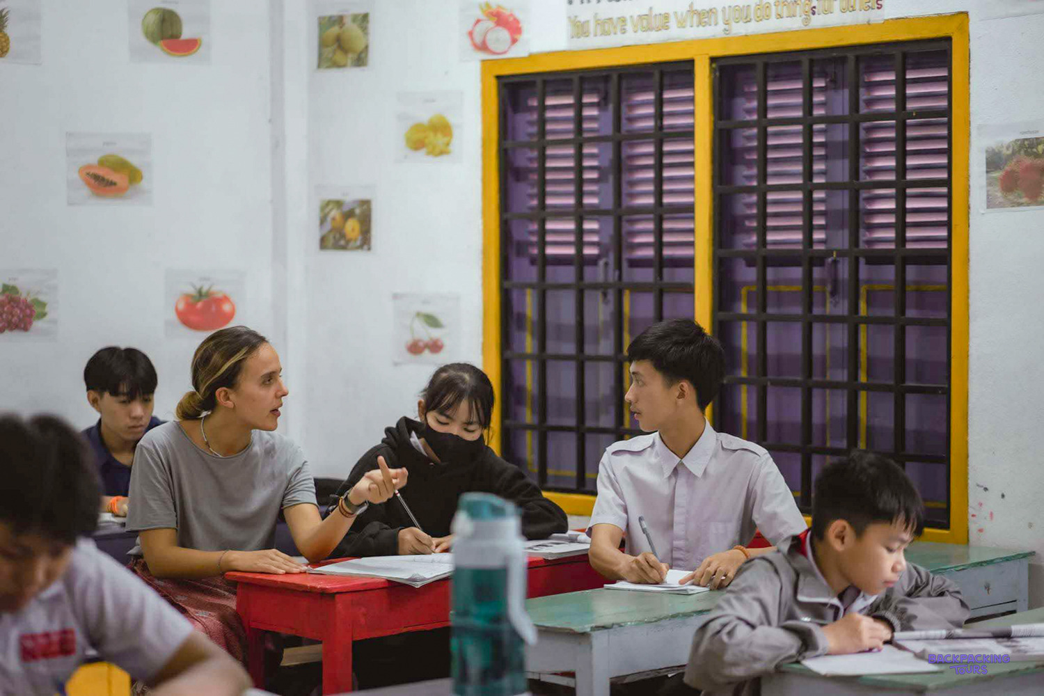 A volunteer explains an exercise to students sitting at red and green desks.