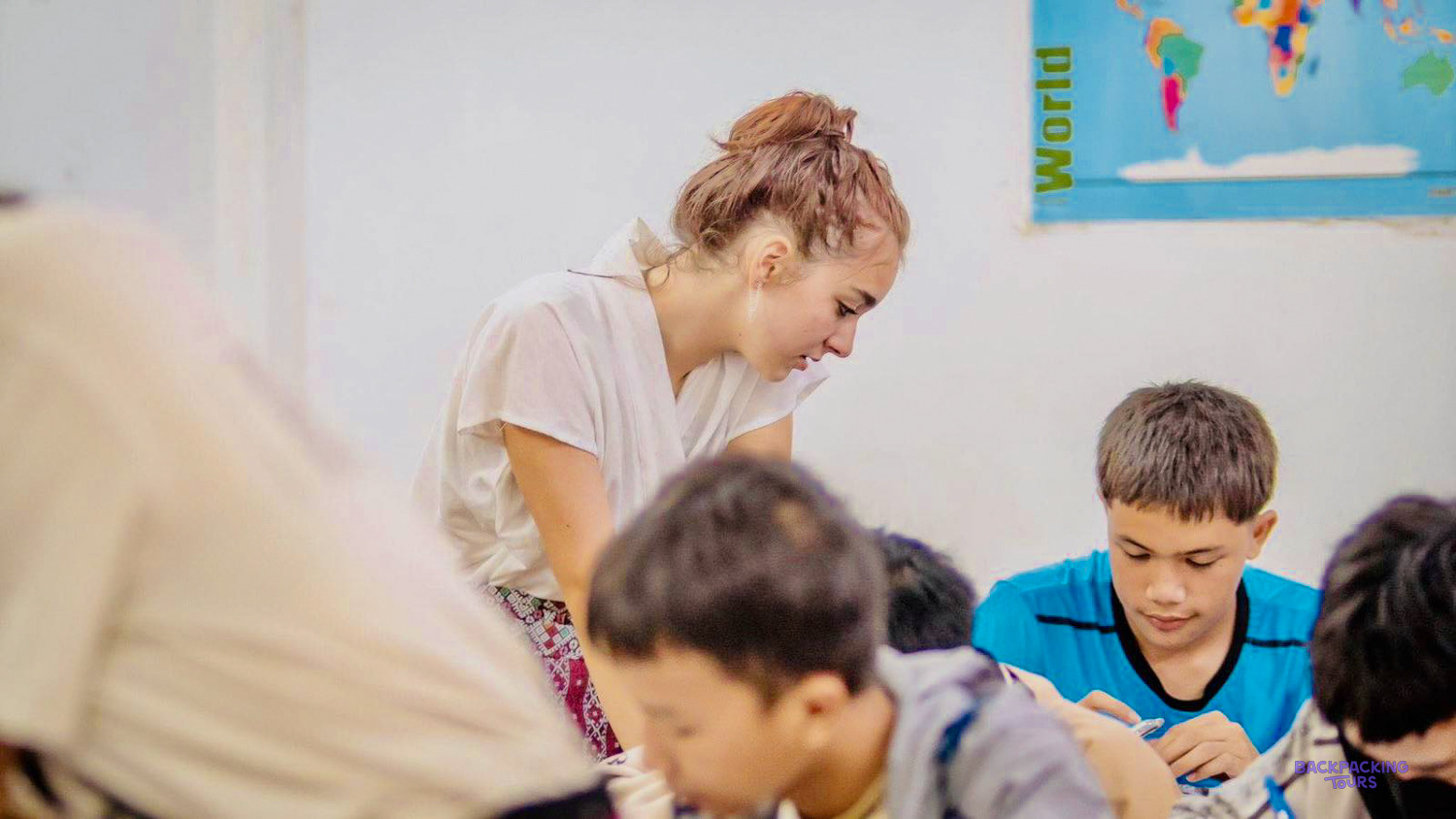 A volunteer leans over to help a boy in a blue shirt with his written work.