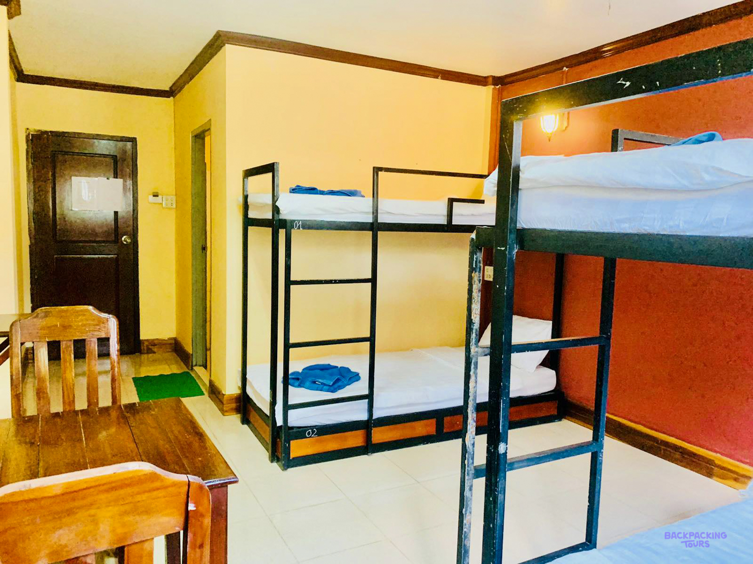 Bunk beds made up with white sheets and blue towels beside a wooden desk in a volunteer room.