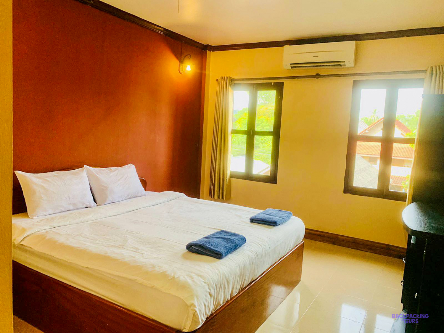 A double room at the volunteer house with a large bed, folded towels and two tall windows.