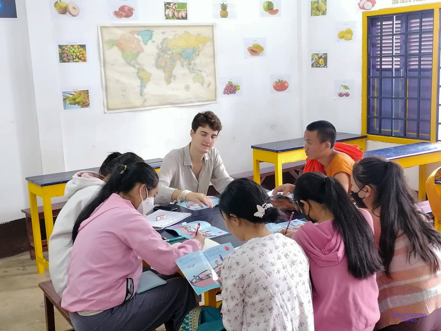 A volunteer works through an English workbook with a small group of students around one desk.