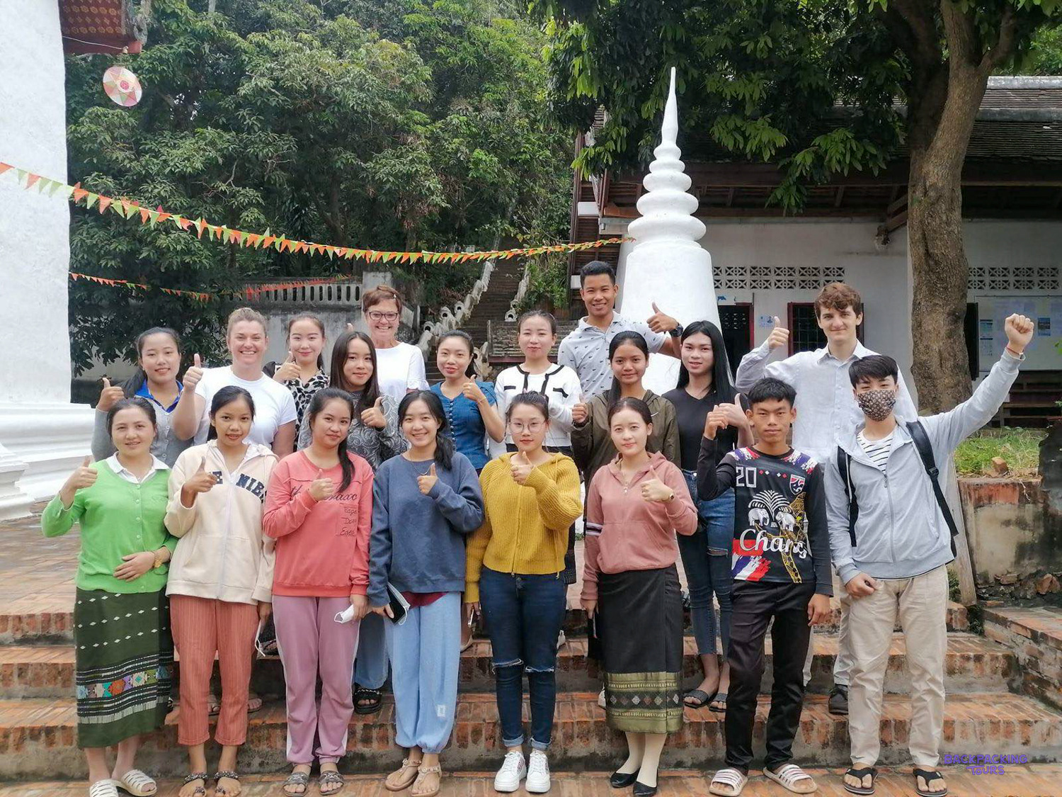 Volunteers and Lao students give a thumbs up together beside a white stupa in Luang Prabang.