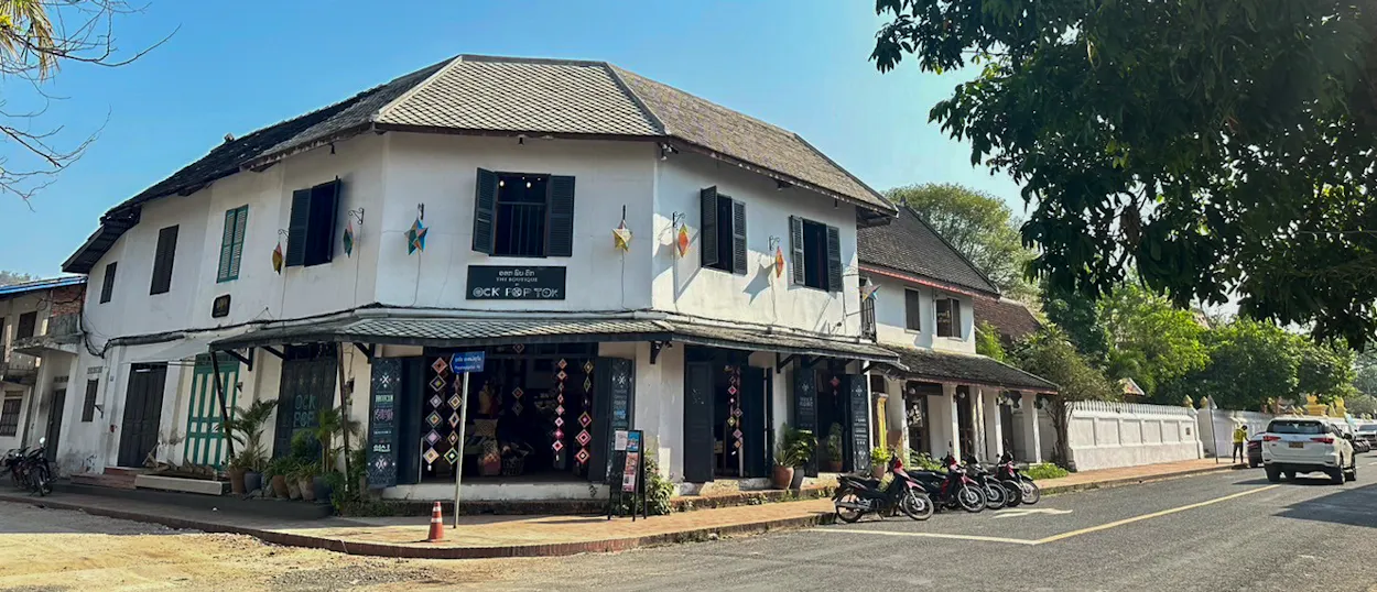 A white two-storey colonial shophouse on a quiet street corner in Luang Prabang's old town.