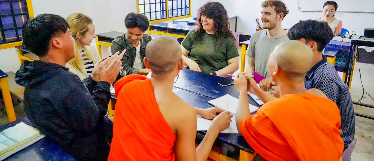 Volunteers chat across a table with young monks and Lao students during a conversation class.
