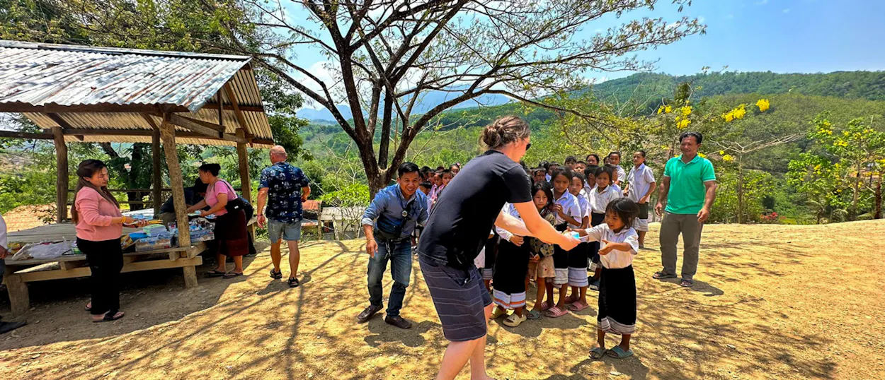 A volunteer hands school supplies to a line of pupils at a hillside village school.
