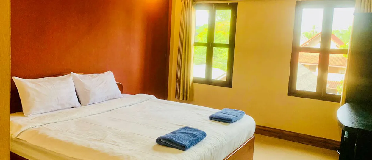 A double room at the volunteer house with a large bed, folded towels and two tall windows.