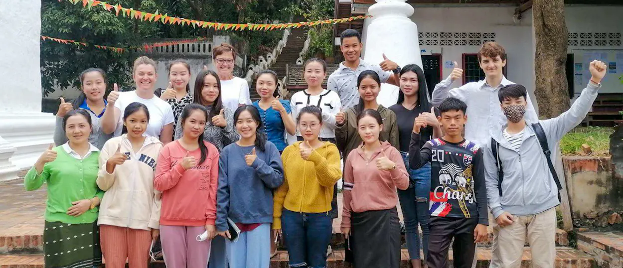 Volunteers and Lao students give a thumbs up together beside a white stupa in Luang Prabang.