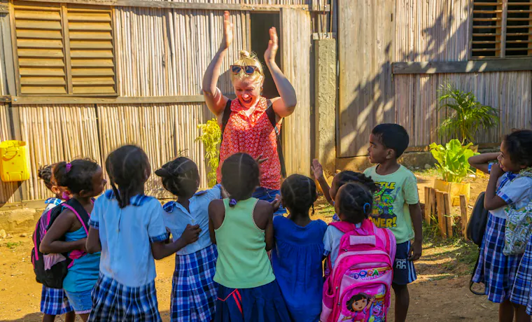 A cheerful volunteer claps hands with smiling children wearing school uniforms in Madagascar.
